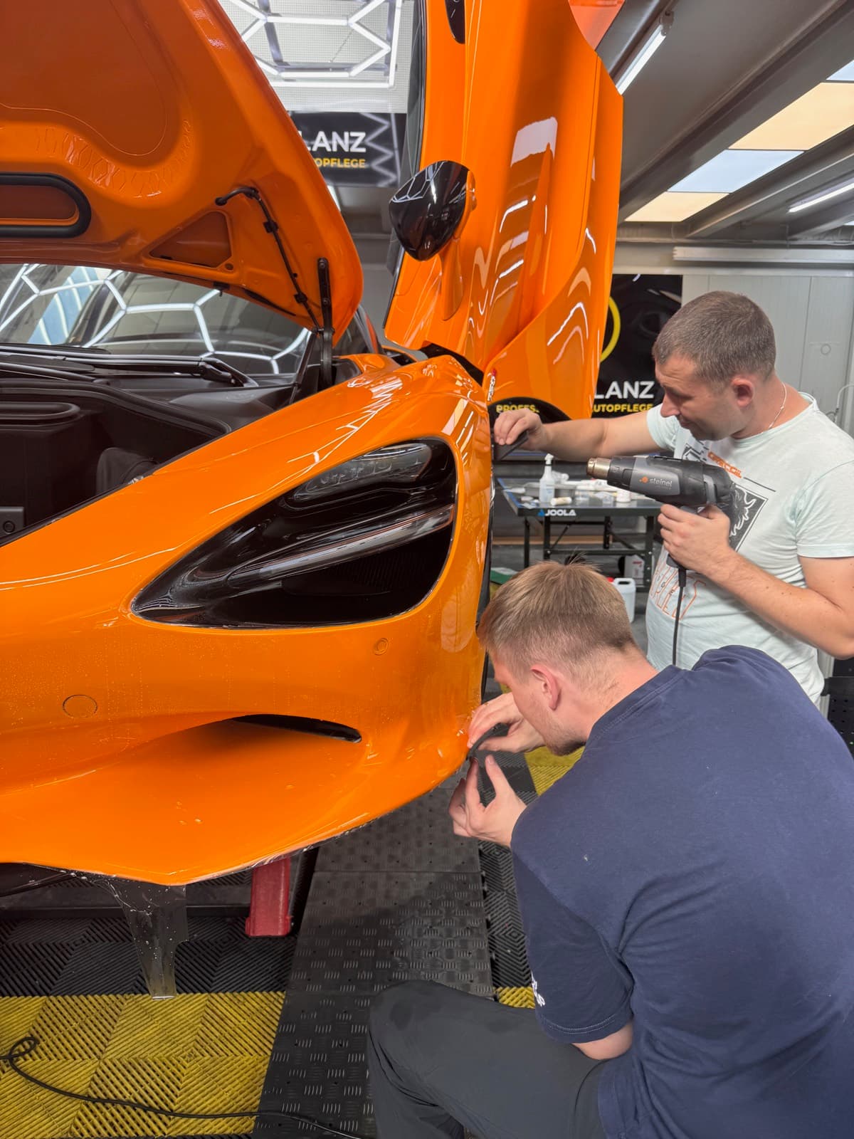 Detailarbeit an der Lackschutzfolie eines orangen McLaren 720S
