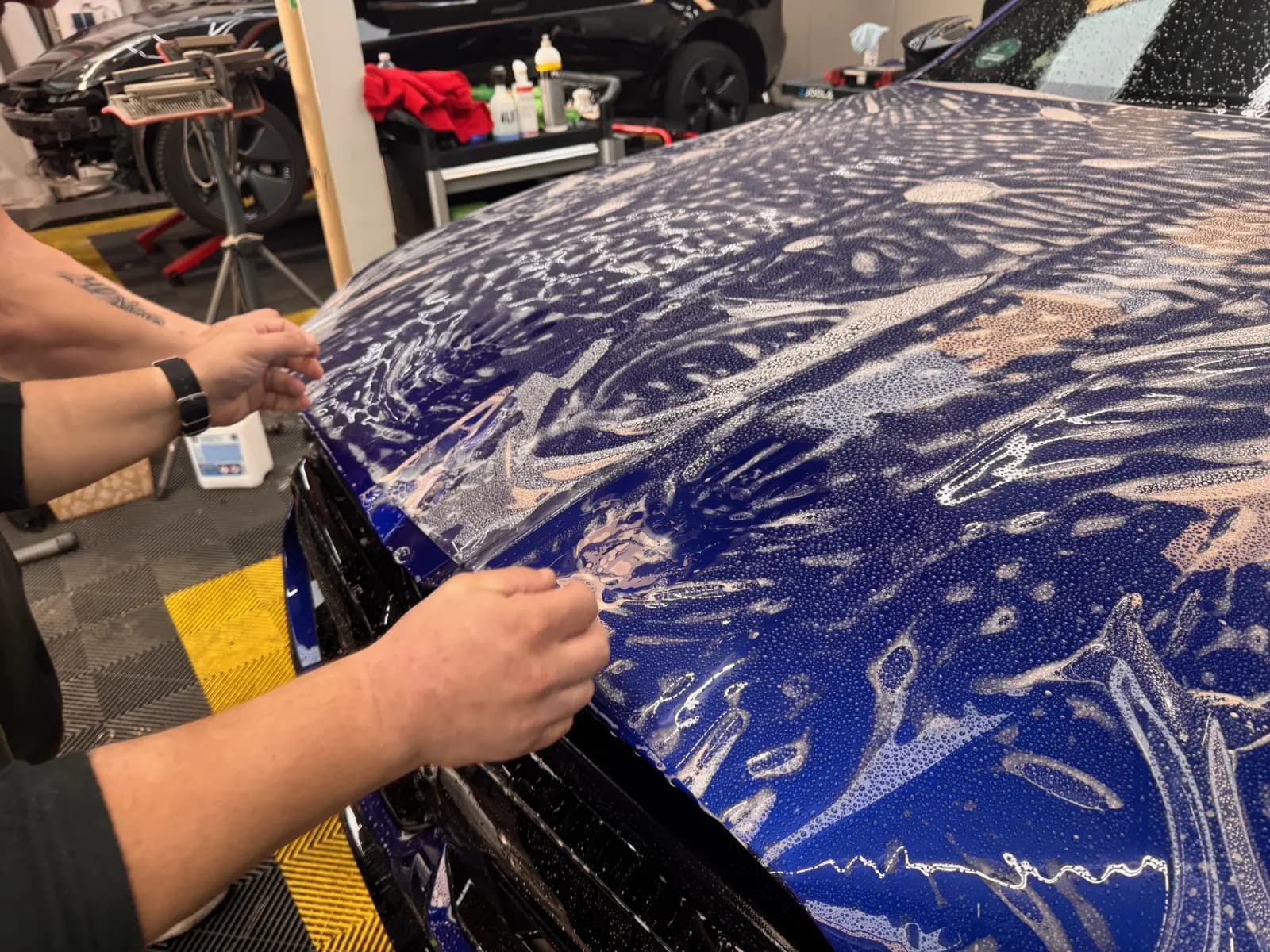 Lackschutzfolie wird von Hand auf einer blauen Motorhaube verlegt